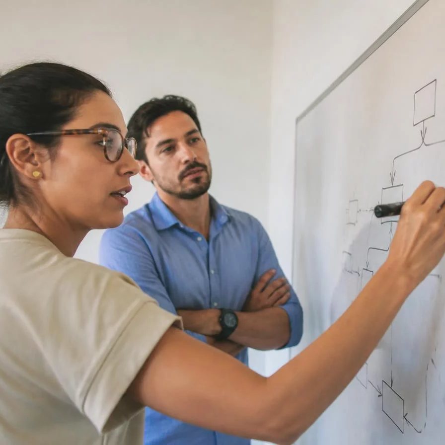 Duas participantes de pé junto ao quadro branco, desenhando as partes de um argumento